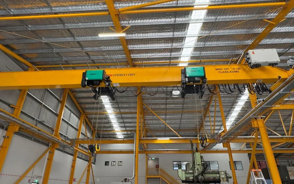 Yellow overhead crane beam with dual hoists and controls in a workshop facility