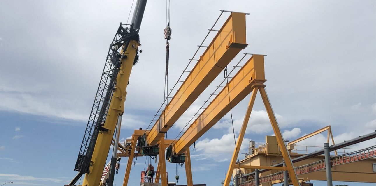 Portal crane installation with a mobile crane lifting a yellow gantry beam