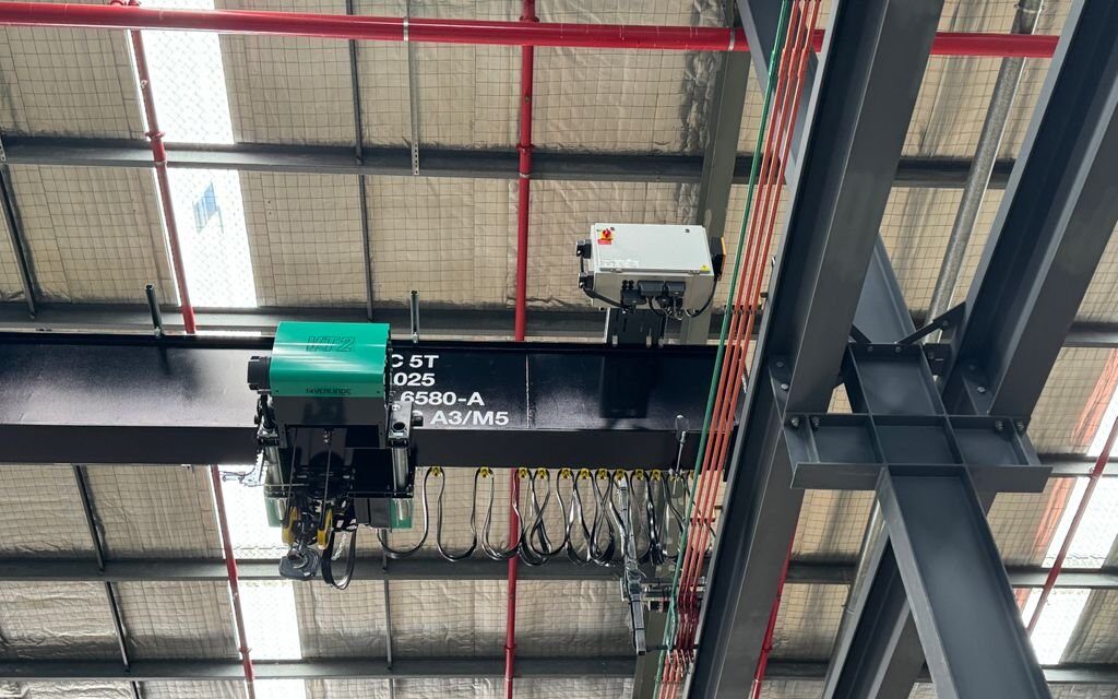 Electric hoist on overhead crane beam with power supply.