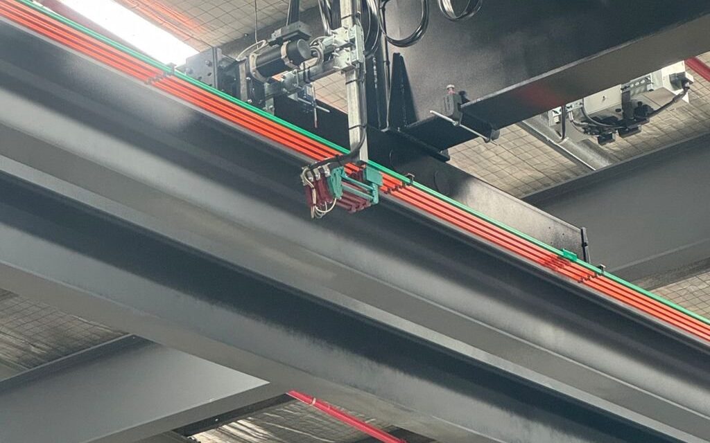 Detailed view of overhead crane power rail and festoon cable carrier.